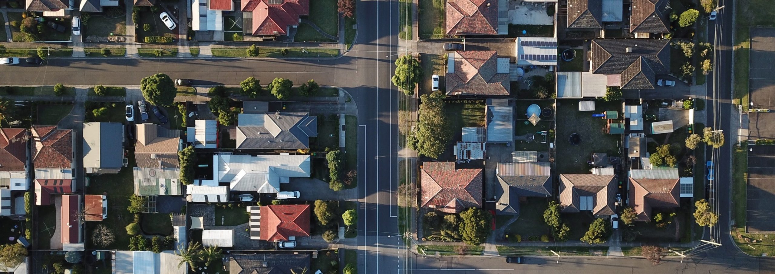 An image that shows a street view of houses in blocks from above. There are many house roofs with a T road dividing them. It represents the view of a suburban neighbourhood from above